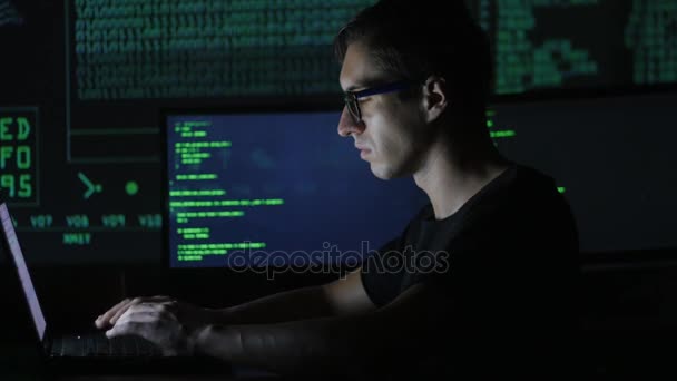 Hacker programmer in glasses is working on computer in cyber security center filled with display screens. — Stock Video