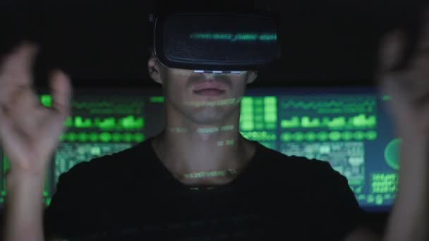 Male hacker programmer uses a virtual reality helmet for programming while green code characters reflect on his face. IT Technologies of the Future. — Stock Video