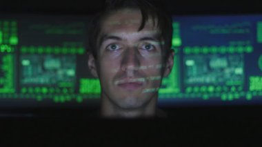 Siber Güvenlik Merkezi'ndeki yüzünde yeşil kod karakterlerini yansıtan iken bilgisayarda çalışan adam hacker programcı göstermek perde ile dolu.