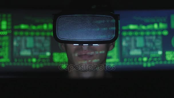Maschio programmatore hacker utilizza un casco realtà virtuale per la programmazione, mentre i caratteri di codice verde riflettere sul suo volto. Tecnologie informatiche del futuro . — Video Stock