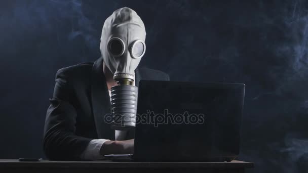 Hombre de negocios en máscara de gas trabajando en el ordenador portátil en la oficina en el humo — Vídeo de stock