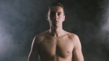 Yakışıklı gömleksiz adam dumanlı çevresindeki koyu arka plan üzerinde ayakta.