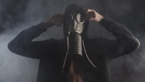 Человек в противогазе раздевается в дымчатой темной комнате — стоковое видео