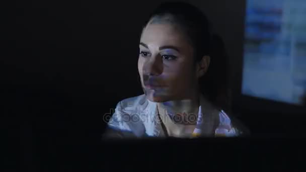Ung kvinna söker information på Internet, sitter vid datorn i ett mörkt rum — Stockvideo