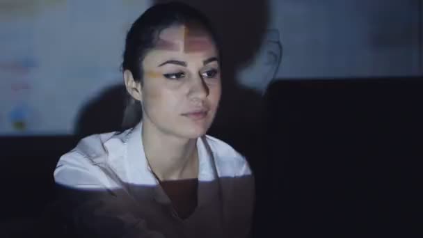 Jonge vrouw is op zoek naar informatie op het Internet, zit op de computer in een donkere kamer — Stockvideo