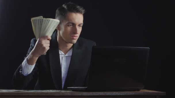 Νεαρός επιτυχημένος επιχειρηματίας με τους λογαριασμούς δολαρίων που στοιβάζονται σε έναν ανεμιστήρα που λειτουργεί σε ένα φορητό υπολογιστή — Αρχείο Βίντεο