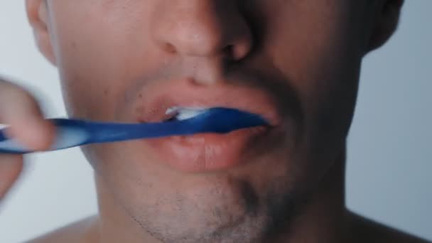 Extremo cerca de la boca de los hombres mientras se cepilla los dientes sobre un fondo blanco aislado — Vídeos de Stock