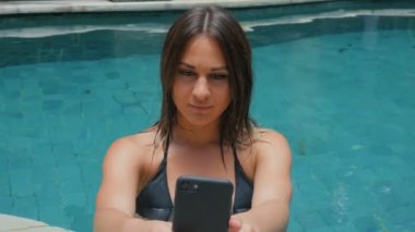 genç kadın bir smartphone bir havuz kenarında kullanır..