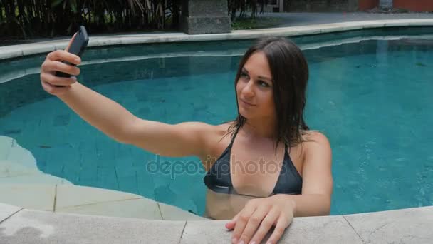 Joven morena haciendo selfie usando smartphone en piscina en vacaciones — Vídeo de stock