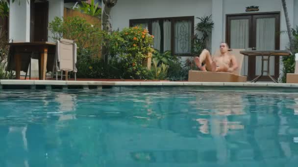 Hombre joven en vacaciones de verano saltando voltear en el agua azul de la piscina para refrescarse en el día soleado caliente. Guy buceando en una piscina vacía en un resort de lujo — Vídeos de Stock