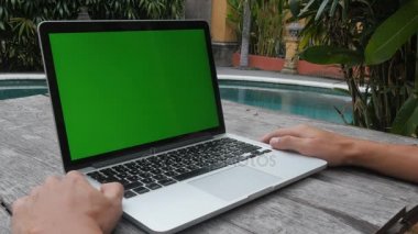 adam laptop yeşil ekran çalışıyor. Açık havuzun temiz. resort adlı çalışması