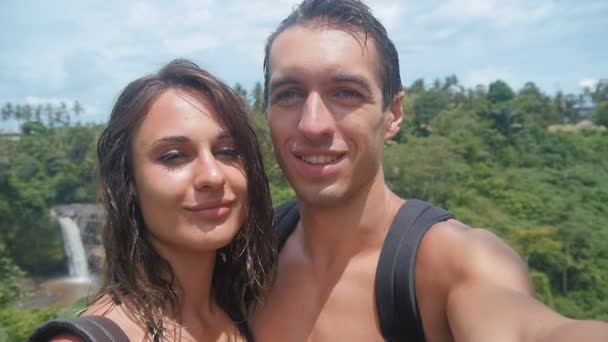Mladý pár pořizování selfie nedaleko krásného vodopádu v džungli v Bali — Stock video