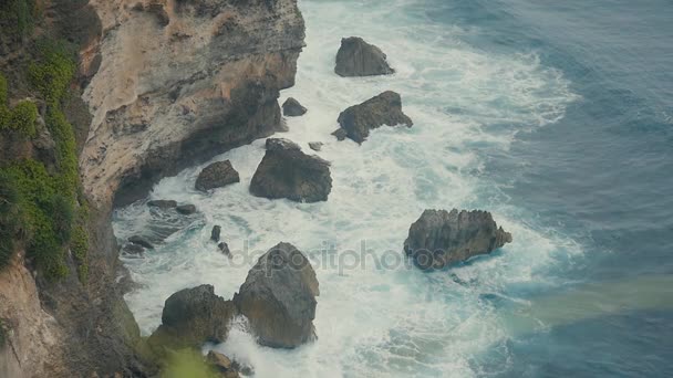 Τα κύματα του ωκεανού σπάσιμο στους πέτρινους βράχους. Εναέρια άποψη του τροπική παραλία Μπαλί, Ινδονησία. Αργή κίνηση — Αρχείο Βίντεο