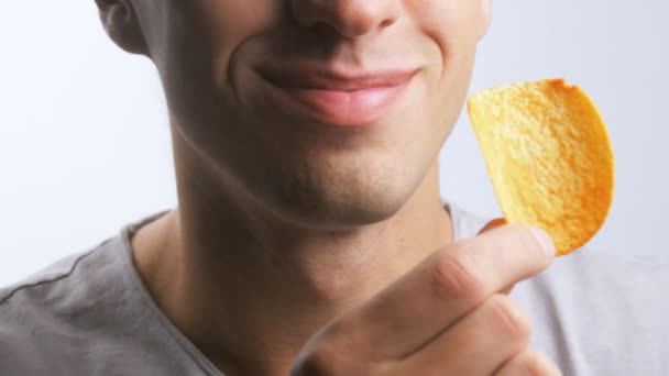 Close-up van een jonge man eet potato chips met plezier op een witte achtergrond — Stockvideo