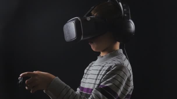Boy использует VR-гарнитуру с наушниками и джойстиком для игры в виртуальную реальность. UHD 4K — стоковое видео