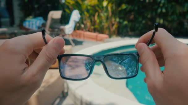 Ego-View: Mann setzt sich im Sommer Sonnenbrille in einem Resort am Pool auf — Stockvideo