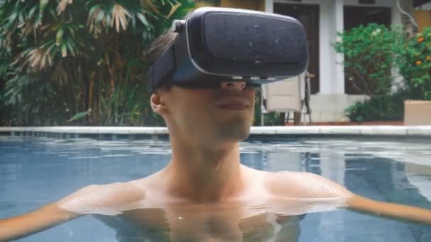 Giovane uomo utilizza occhiali di realtà virtuale mentre nuota in piscina. Ragazzo ottenere esperienza nell'utilizzo VR-headset in estate in vacanza Video Stock Royalty Free