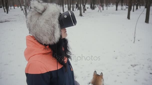 Bela jovem fêmea usa óculos vr no parque de inverno nevado. Mulher bonita recebe experiência usando óculos de realidade virtual moderna — Vídeo de Stock