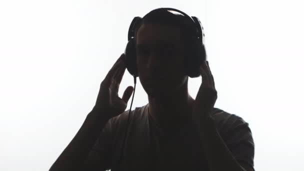 Silhouette eines Mannes, der Kopfhörer aufsetzt und isoliert auf weißem Hintergrund Musik hört — Stockvideo