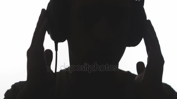 Close-up van silhouet van Man hoofdtelefoon op te zetten en het luisteren muziek geïsoleerd op witte achtergrond — Stockvideo
