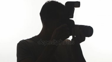 Fotoğrafçı yakın çekim silüeti. Genç adam beyaz arka plan üzerinde izole Dslr fotoğraf makinesi ile fotoğraf çeker