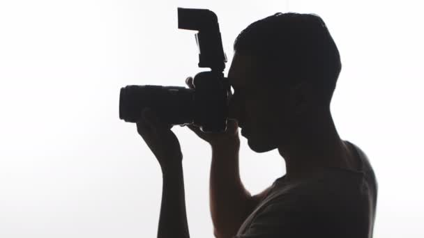 Fotografo Silhouette primo piano. Giovane uomo scatta foto con fotocamera DSLR isolato su sfondo bianco — Video Stock
