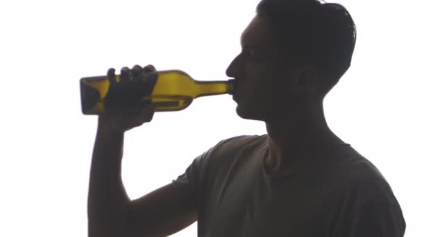 Silueta del joven bebe alcohol de una botella aislada sobre fondo blanco — Vídeos de Stock