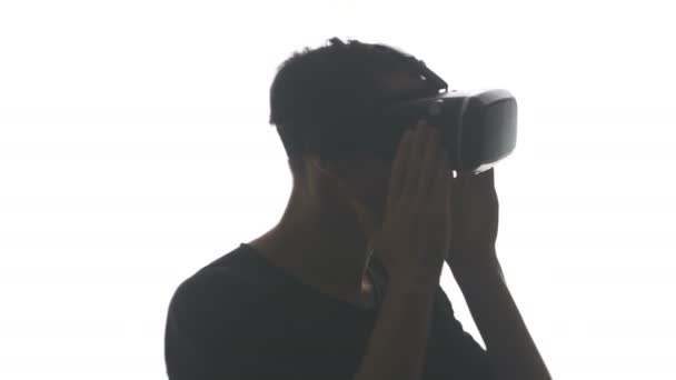 Silhouette di un giovane uomo in cuffia che acquisisce esperienza nell'utilizzo di cuffie VR, isolate su sfondo bianco — Video Stock