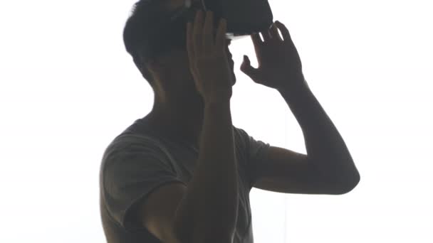 Силуэт молодого человека в наушниках, получающего опыт использования VR-гарнитуры, изолированного на белом фоне — стоковое видео