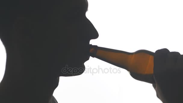 Close up silhouette of a young man drinking beer from a bottle isolated on white background — Stock Video