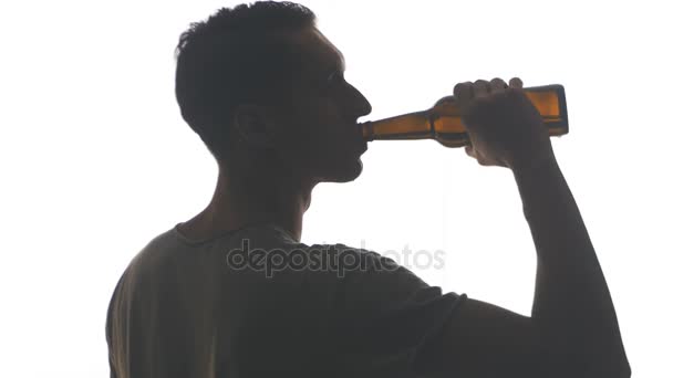 Silhouet van een jonge man bier drinken uit een fles geïsoleerd op witte achtergrond — Stockvideo