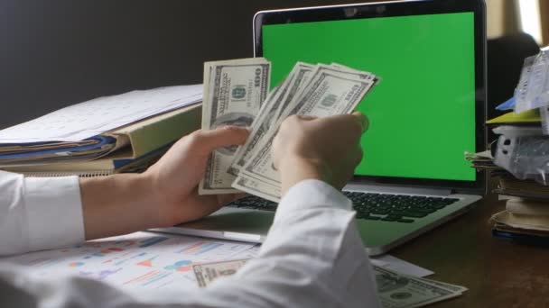 Businessman at workplace counting Many American 100 bills. oncept of salary or making money. Laptop with a green screen on the desk — Stock Video