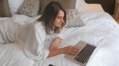 Genç kadın yatakta yatarken ve dizüstü bilgisayarda çalışma bornoz