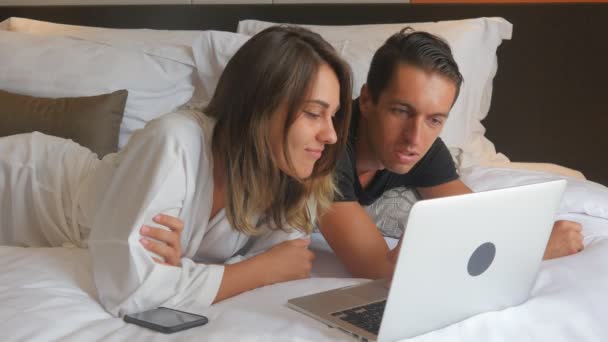 Young couple in bathrobe lying on bed and working on laptop — Stock Video