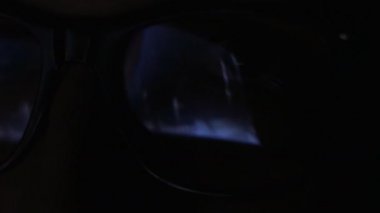 Yakın çekim yansıma geceleri bir film izlerken bir adamın gözlük. Çift pozlama video izlerken biri. Makro
