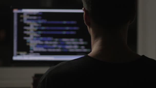 Programmer from behind and programming code on computer monitor at night in a dark room — Stock Video