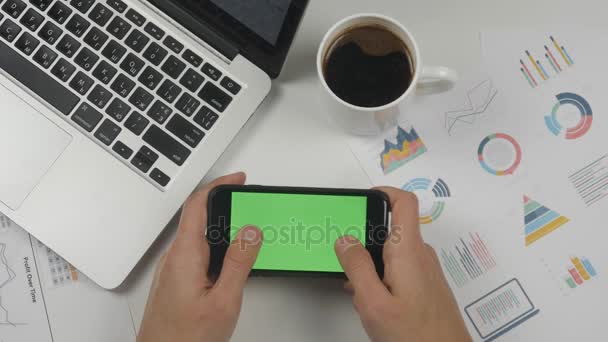 Ο άνθρωπος παίζει το παιχνίδι στο smartphone με πράσινη οθόνη στο φόντο λευκό γραφείο τραπέζι. — Αρχείο Βίντεο