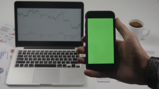 Uomo d'affari che utilizza smartphone con schermo verde su tavolo da ufficio bianco con laptop sullo sfondo. Vista dall'alto. Pagine a scorrimento mani maschili, zoom, toccando il touch screen . — Video Stock