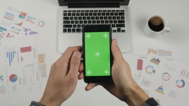 商人使用智能手机与绿色屏幕在白色的办公室表背景。顶部视图。男性手滚动页面, 变焦, 触摸屏上点击。办公台背景 — 图库视频影像