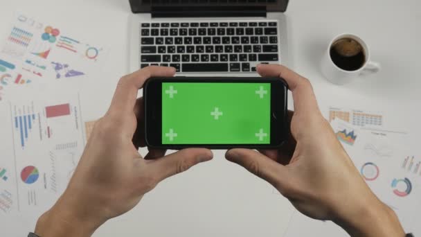 Mann mit Smartphone Touch mit grünem Bildschirm Chroma-Taste in horizontaler Position auf weißem Bürotischhintergrund. Bürokram auf dem Schreibtisch. — Stockvideo