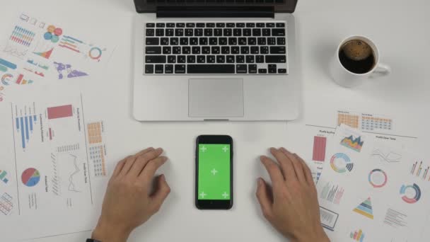 Empresário usando smartphone com tela verde no fundo da mesa do escritório branco. Vista superior. Mãos masculinas rolando páginas, zoom, tocando na tela sensível ao toque. Escritório de fundo — Vídeo de Stock