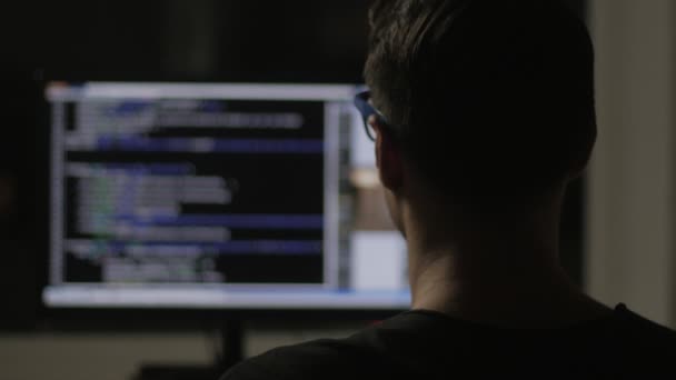 Programmeur par derrière et code de programmation sur écran d'ordinateur la nuit dans une pièce sombre — Video