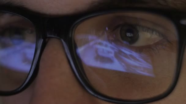 Reflexão close-up em óculos: Gamer joga um jogo de vídeo em um computador em uma sala escura — Vídeo de Stock