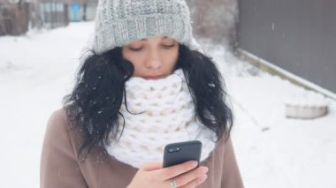 Genç Beyaz karlı kış döneminde bir akıllı telefon kullanan kadın.