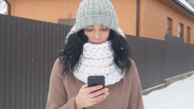 Genç Beyaz karlı kış döneminde bir akıllı telefon kullanan kadın.