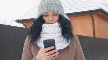 Genç Beyaz karlı kış döneminde bir akıllı telefon kullanan kadın.