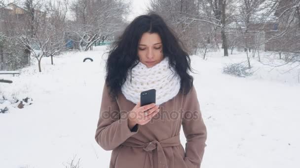 Ung kaukasisk kvinna med en smartphone i snöiga vintern. — Stockvideo