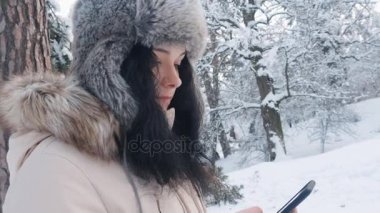 Karlı kış ormanda bir smartphone kullanarak sıcak şapka içinde genç beyaz kadın yakın çekim