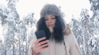 Karlı kış ormanda bir smartphone kullanarak sıcak şapka içinde genç Kafkas kadın