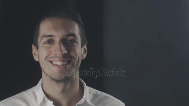Молодой счастливый человек в белой рубашке смотрит в камеру и улыбается — стоковое видео